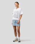 Model wearing white Silverstone Core T Shirt with a geometric front print and Union Jack sleeve patch, paired with a light denim skirt