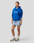 Three-quarter view of a woman in a blue Silverstone Core Hoodie with a white coordinates graphic on the chest