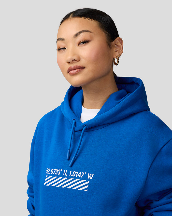 Model wearing blue Silverstone Core Hoodie with hood up and coordinates graphic on the chest.