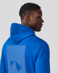 Back view of a man in a blue Silverstone Core Hoodie showing a large white line art graphic on the back.