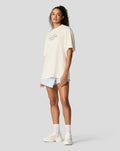 Model wearing unisex Silverstone 75 Years Oversized T Shirt in Egret with light denim shorts.
