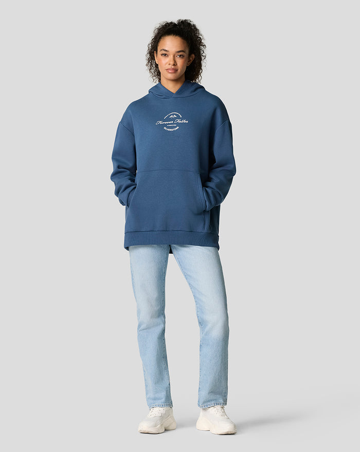 Model wearing oversized Silverstone 75 Years hoodie in Sargasso Sea blue with front pocket.