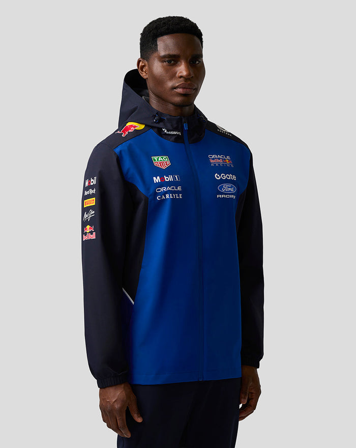 Model wearing a blue and navy Oracle Red Bull Racing Teamline water resistant jacket with a hood, branding on chest and sleeves.