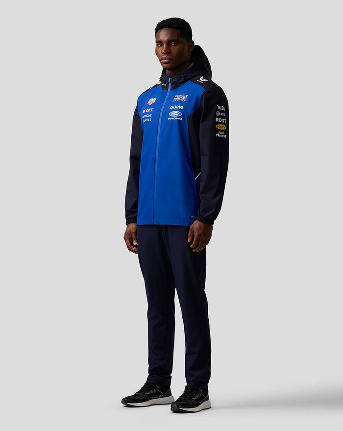 Front view of a male model in a blue and navy Oracle Red Bull Racing Teamline water resistant jacket with hood and sponsor logos