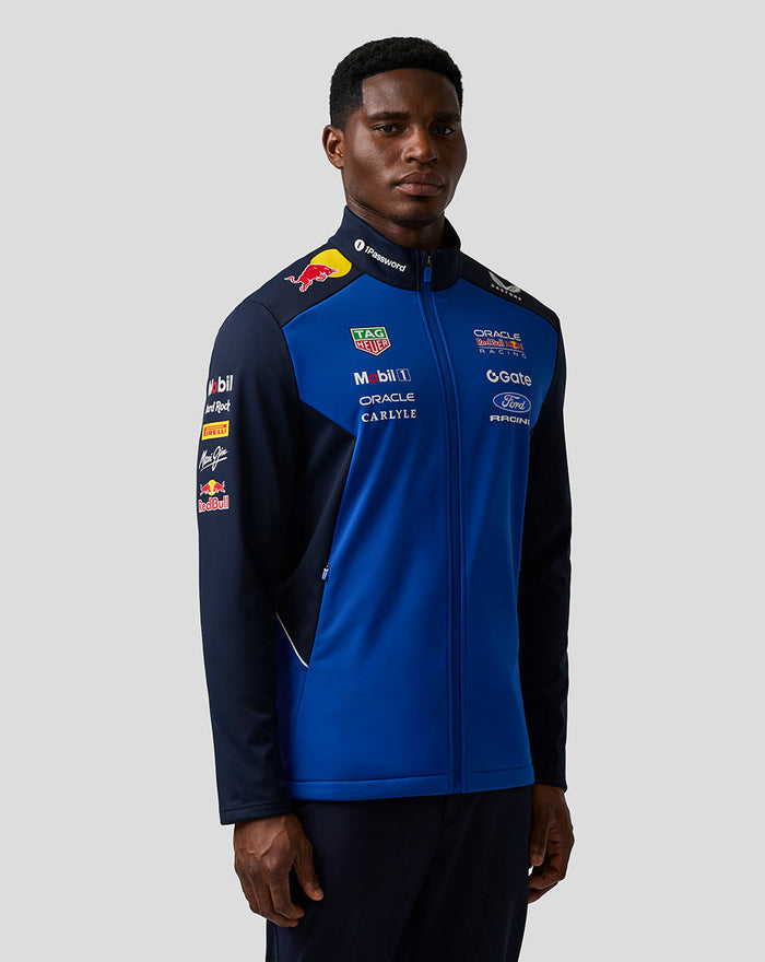 Front three quarter view of a male model wearing the Oracle Red Bull Racing Teamline Soft Shell Jacket in night sky blue.