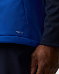 Close-up of blue soft shell fabric with water droplets and Protek branding.