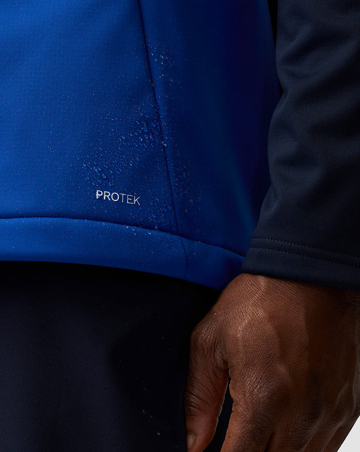Close-up of blue soft shell fabric with water droplets and Protek branding.