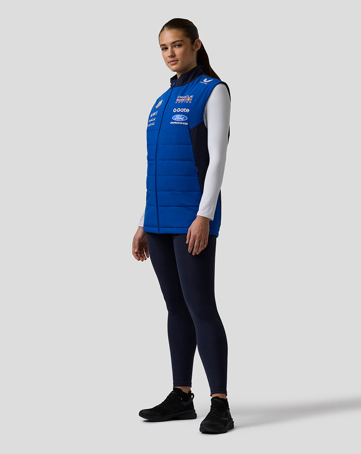 Side profile of female model wearing blue Oracle Red Bull Racing Teamline Gilet over a white long sleeve with logos on the chest