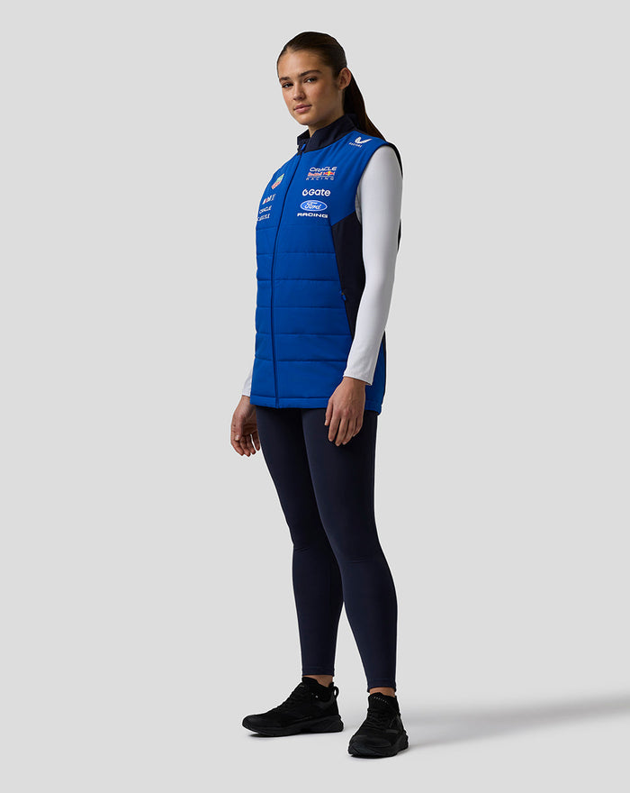 Side profile of female model wearing blue Oracle Red Bull Racing Teamline Gilet over a white long sleeve with logos on the chest
