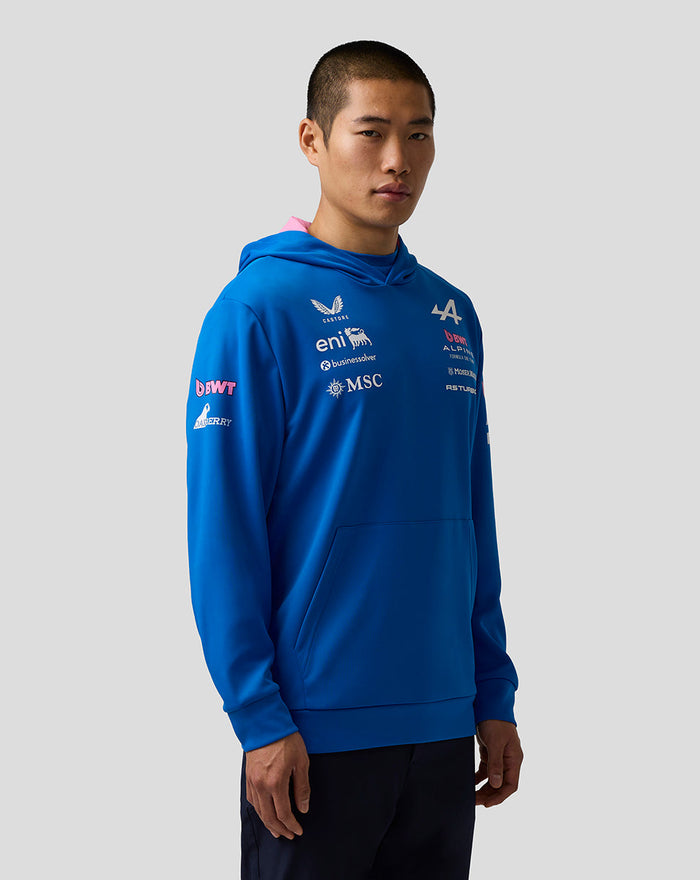Three-quarter view of a man in a blue BWT Alpine hoodie with multiple chest and sleeve logos and a pink hood lining.