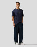 Male model wearing navy night sky Max Verstappen logo T shirt with relaxed fit denim jeans and white sneakers