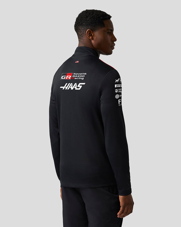 Back view of a model in a black Haas Team Quarter Zip Midlayer with Haas and Toyota Gazoo Racing logos and a USA flag at the hem