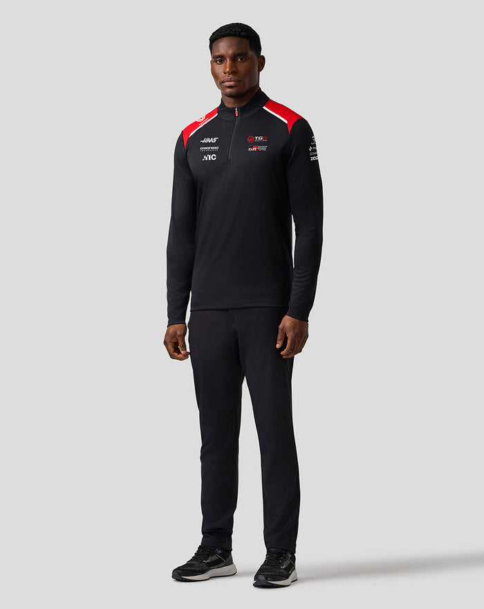 Male model wearing Official Haas Team Quarter Zip Midlayer in black with red shoulder panels and sponsor logos on the chest