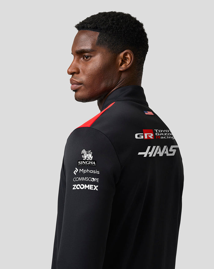 Back view of a model wearing a black Haas Team Quarter Zip Midlayer with back logos and sleeve branding for Singha Mphasis Commscope Zoomex