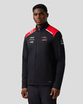 Male model wearing Haas Team unisex soft shell jacket in black with red shoulder panels and front branding.