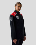 Female model wearing Haas Team unisex soft shell jacket in black with red shoulder panels and logos on chest and sleeve.