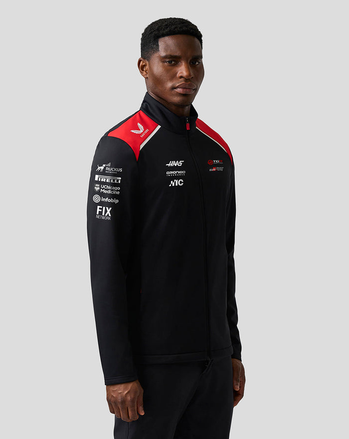 Model wearing Official Haas Team Unisex Soft Shell Jacket in black with red shoulder panels and front zip.