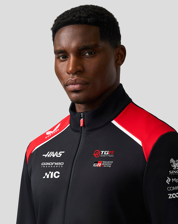 Close up of a male model wearing black Haas Team Soft Shell Jacket with red shoulder panels.