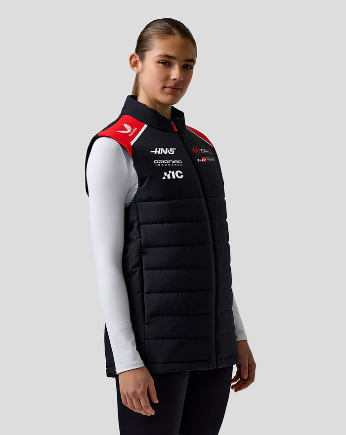 Female model wearing Haas Team Gilet in black quilted design with red shoulder panels shown in three-quarter profile.