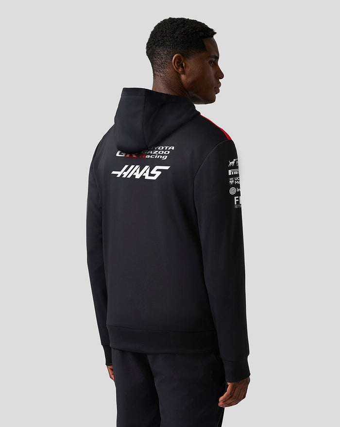 Rear view of a model wearing a black Official Haas Team pullover hoodie with a large white Haas logo on the back.