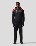 Full front view of a man wearing a black Haas Team pullover hoodie with red shoulder panels and sponsor logos on the chest.