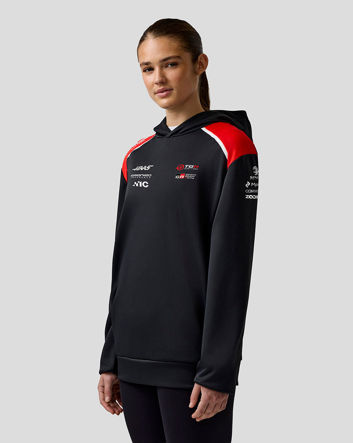 Female model wearing Official Haas Team Unisex Pullover Hoodie in black with red shoulder panels and chest logos.