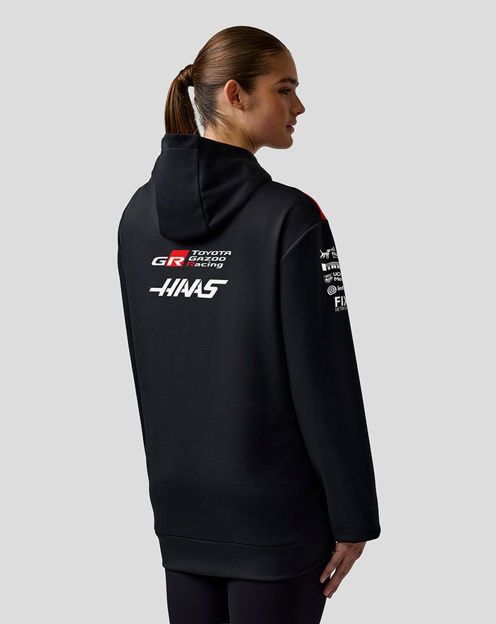 Profile view of a person in a black Haas Team hoodie with red shoulder panels and sponsor logos on the sleeve.