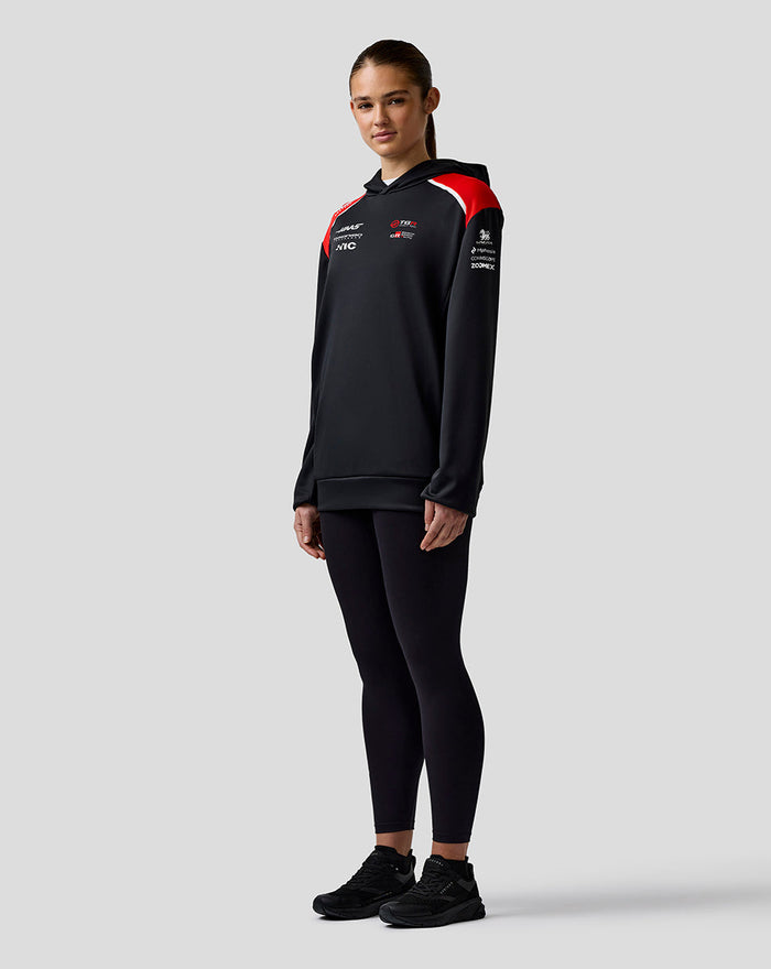 Female model wearing Official Haas Team Unisex Pullover Hoodie in black with red shoulder panels against a light gray backdrop