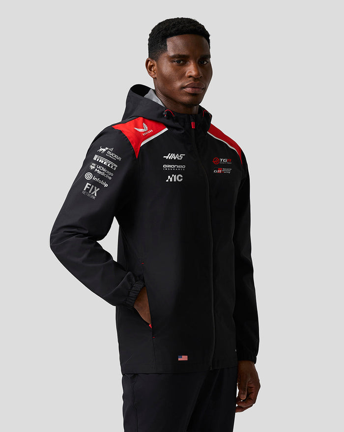 Male model wearing Haas Team water resistant jacket in black with red shoulder panels hood and front zip branding