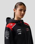 Female model wearing Haas Team water resistant jacket in black with red shoulder panels hood and front branding