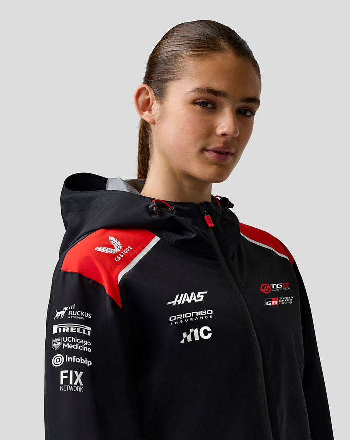 Female model wearing Haas Team water resistant jacket in black with red shoulder panels hood and front branding