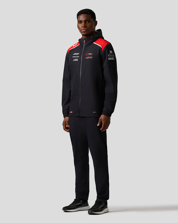 Front view of black hooded Haas Team water-resistant jacket with red shoulders full front zip and branding.