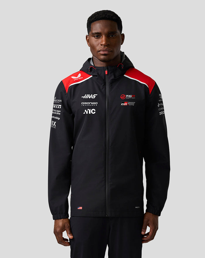 Male model wearing Haas Team Water Resistant Jacket with red shoulder panels, hood, and front zip.