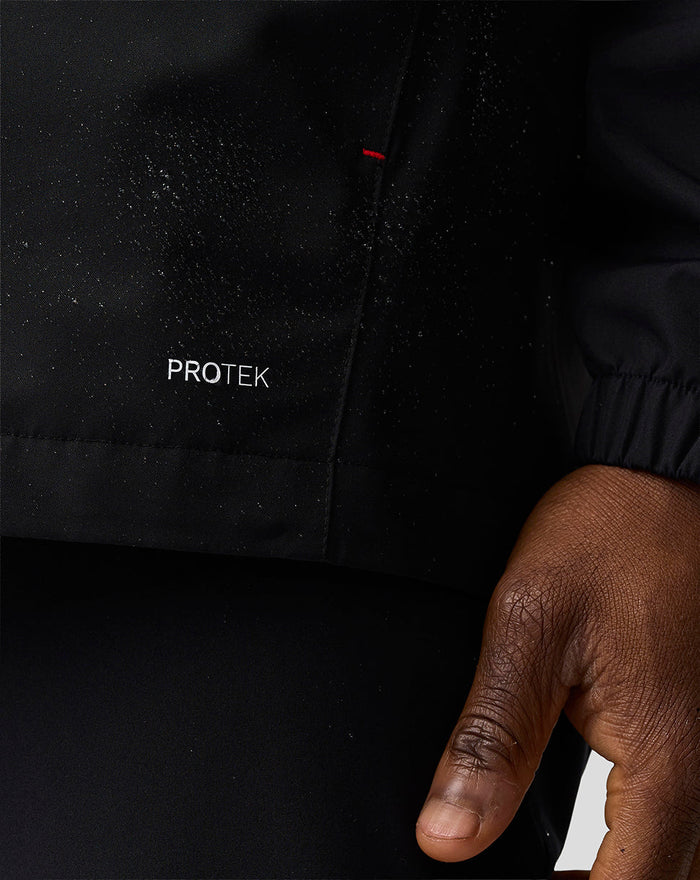 Haas Team water resistant jacket close up showing PROTEK logo on black fabric with red stitch detail