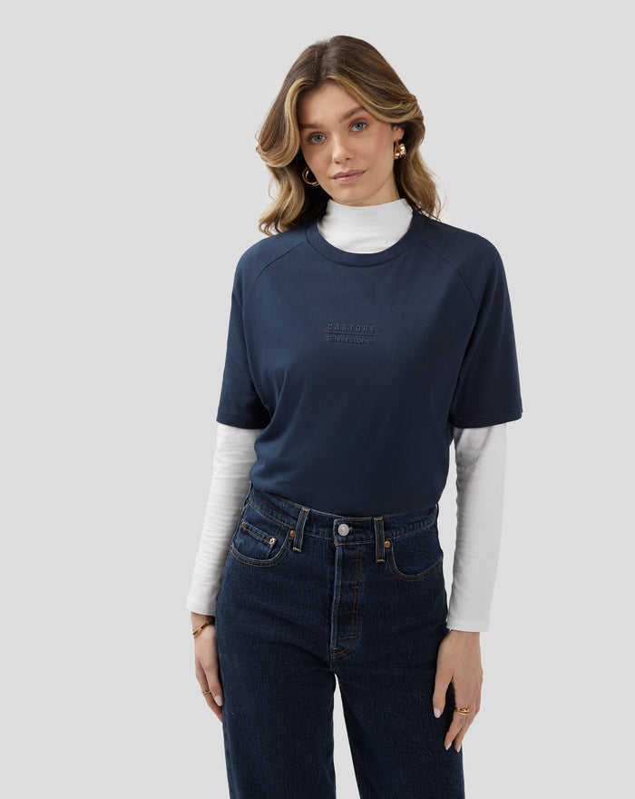 Female model in navy short sleeve T shirt layered over a white turtleneck, showing the chest logo.