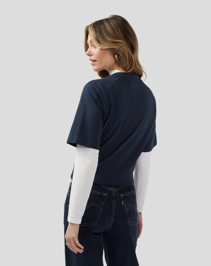 Side profile of a woman wearing a navy unisex short sleeve tee with a back neck logo and white layer underneath