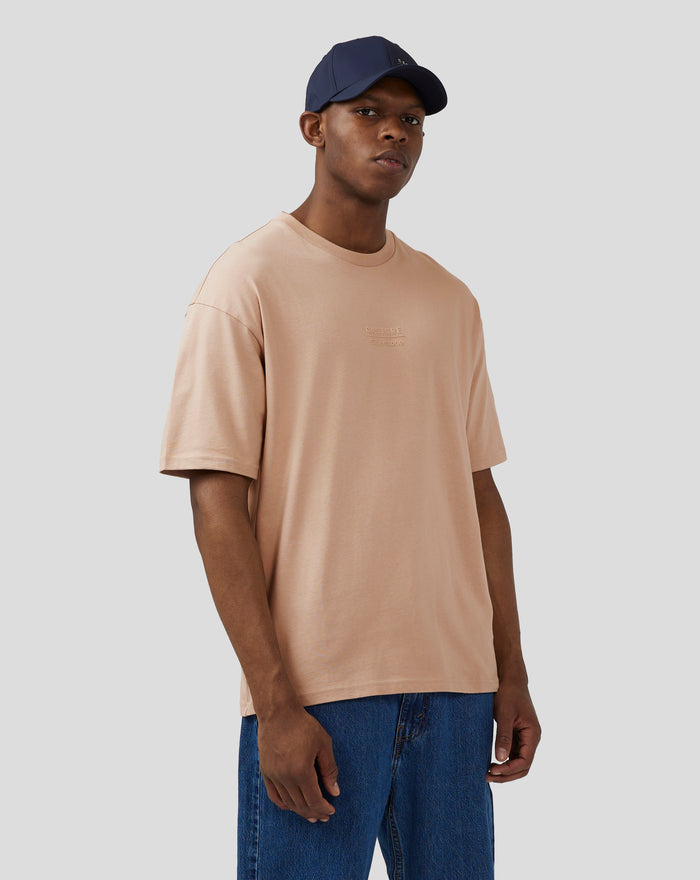 Front view of a model in a doeskin oversized tee with embossed Silverstone logo on the chest and a navy cap