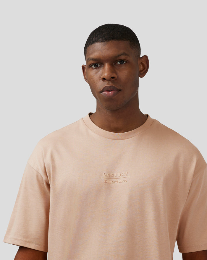 Portrait of a male model wearing a doeskin Silverstone x Castore short sleeve tee with embossed branding on chest and back.