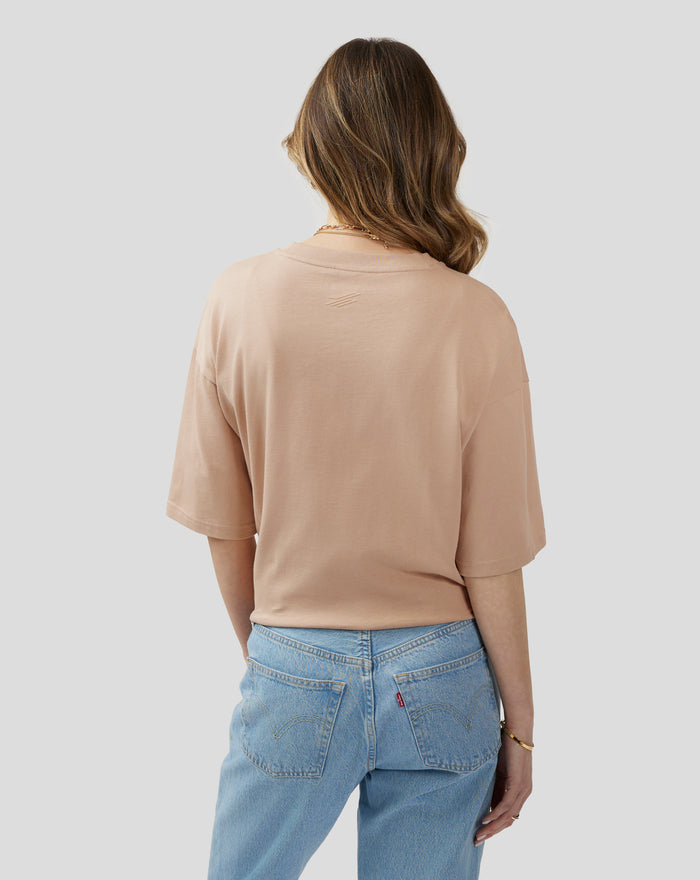 Back view of a model in a doeskin oversized tee showing the small back neck logo