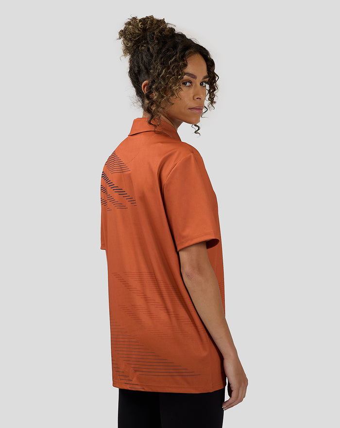 Three-quarter back view of orange rust polo with navy graphic lines along the back and lower hem