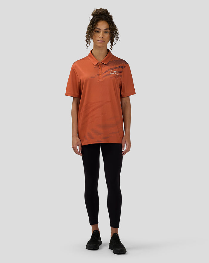 Front view of model wearing orange rust Castore Silverstone polo with diagonal navy stripes and chest logo