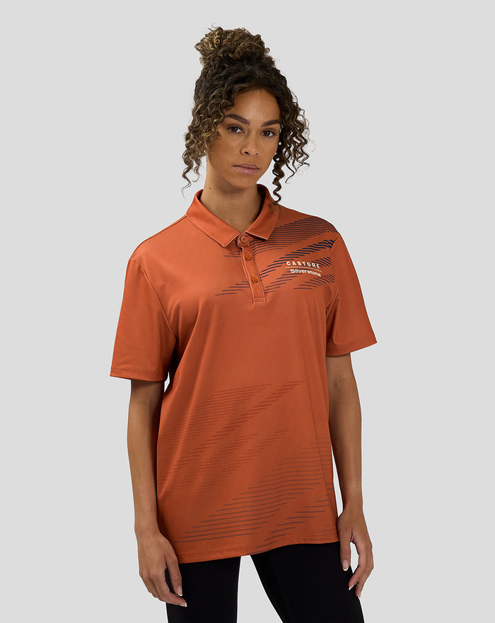 Front view of orange rust unisex Silverstone x Castore polo with navy sublimated line graphics across the chest
