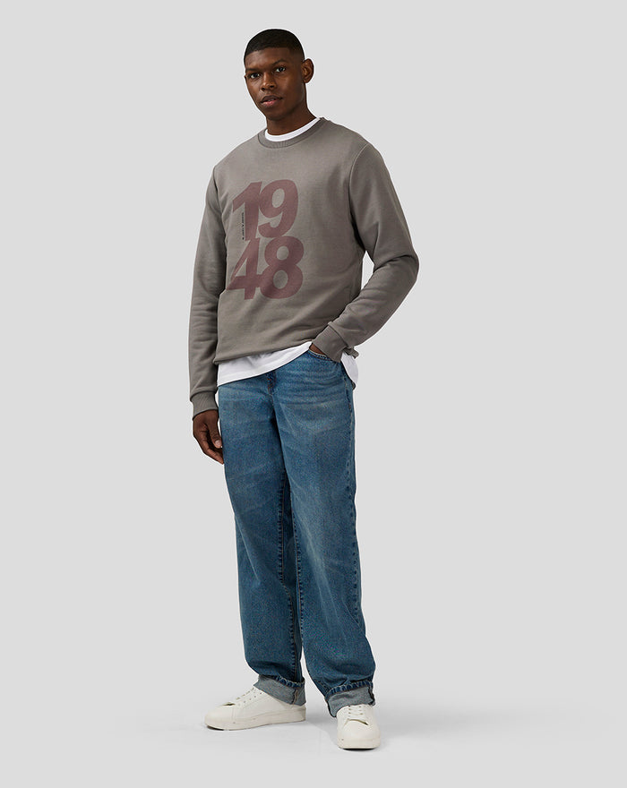 Male model in charcoal Silverstone Core Sweatshirt with 1948 graphic layered over a white tee with blue jeans and white sneakers