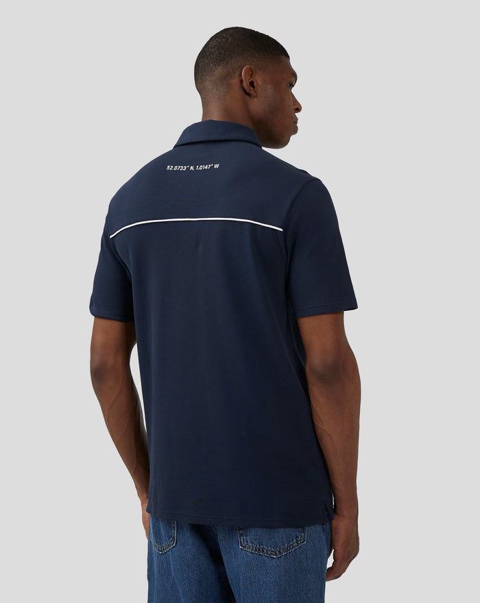 Back view of navy polo with white piping and coordinates printed on the upper back.