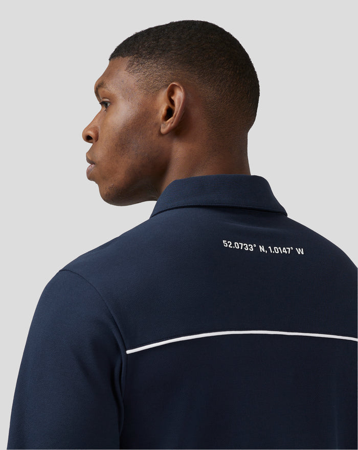 Profile view of a man wearing a dark navy polo with white shoulder piping and coordinates printed on the back.