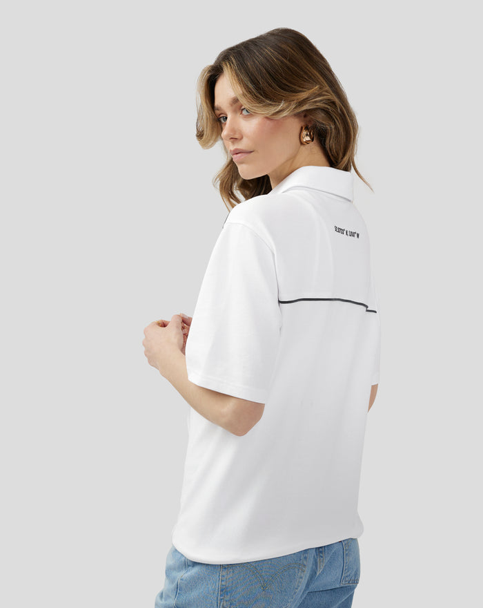 Rear three-quarter view of a white polo with coordinates printed on the back and navy piping along the back seam