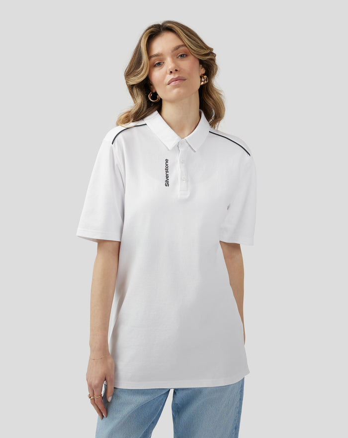 Female model wearing a white Silverstone Core Polo with navy piping on the shoulder seam against a gray background.