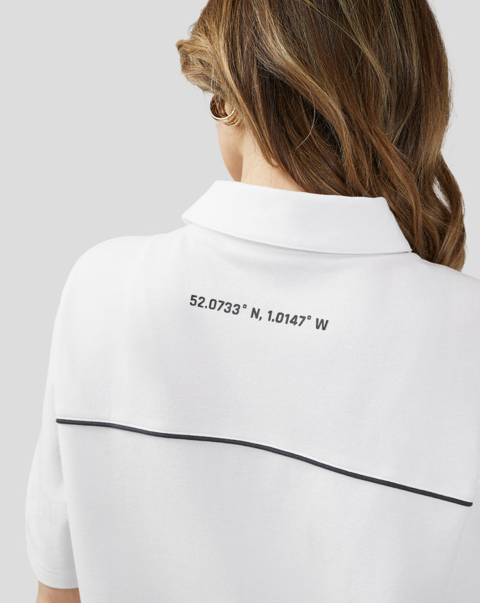 Back view of a Brilliant White unisex polo shirt with coordinates printed on the upper back and dark piping along the hem