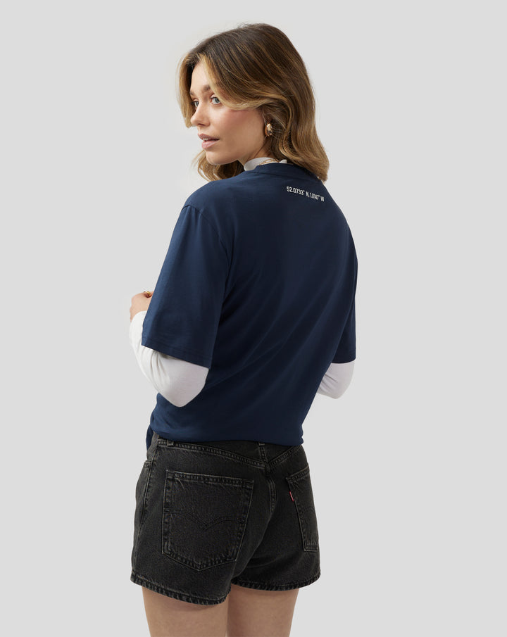 Back view of a woman wearing a navy Silverstone Core T-Shirt with coordinates printed on the upper back.