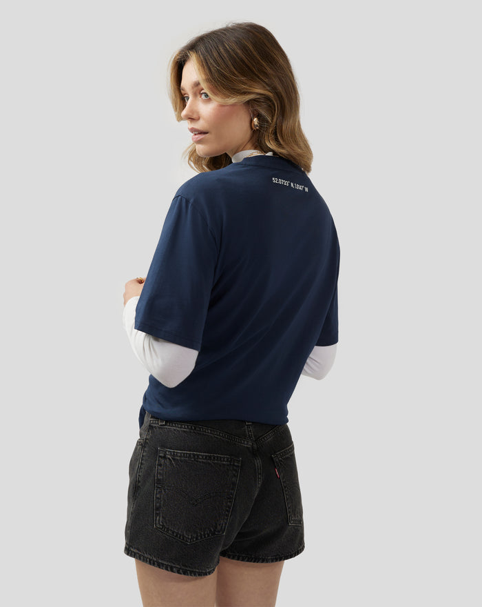 Back view of a woman wearing a navy Silverstone Core T-Shirt with coordinates printed on the upper back.